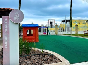 Ein Spielplatz mit einem roten Spielhäuschen, einem eingezäunten Bereich und einem Schild mit der Aufschrift 'PARQUE INFANTIL'.