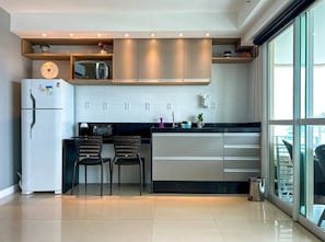 A modern kitchen with a refrigerator, microwave, and two chairs. - Studio com Varanda e Piscina| Beira Mar no Recreio (Rio de Janeiro)