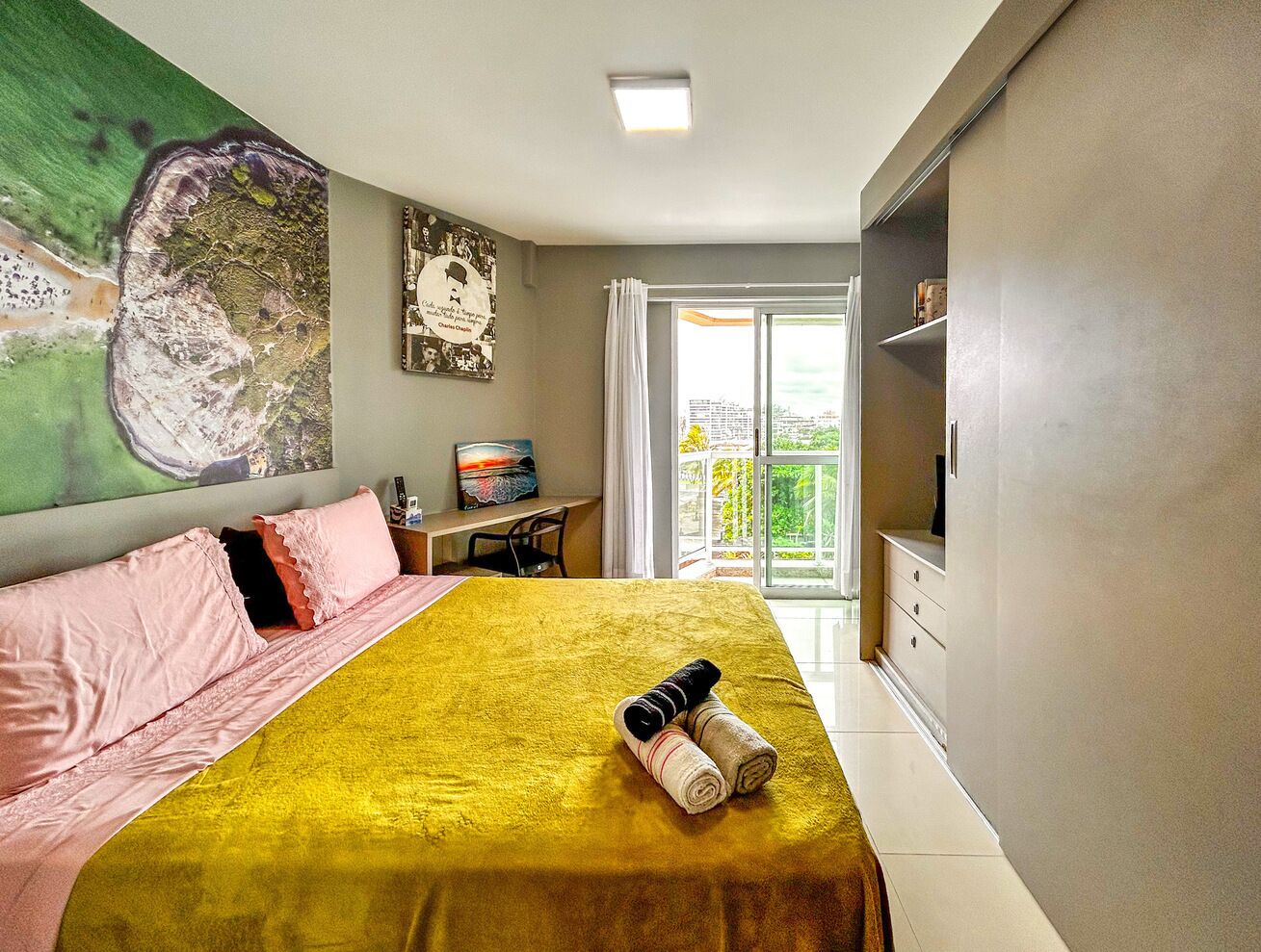 Quarto de hotel com cama, escrivaninha, cadeira, televisão e varanda com vista.