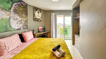 Quarto de hotel com cama, escrivaninha, cadeira, televisão e varanda com vista.