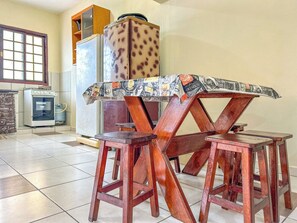 A dining area with a wooden table and stools, a refrigerator, and a window. - Casa c churrasqueira próx à Praia Jardim Real/SP (Praia Grande)