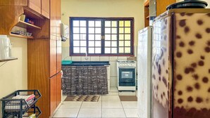 Une cuisine de taille réduite avec des meubles de rangement en bois, une fenêtre avec des stores, un réfrigérateur à motifs et une cuisinière.