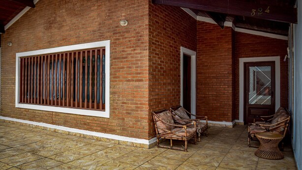 A covered outdoor area with a brick wall, a window with vertical bars, and wicker furniture. - Ótima casa com Wi-Fi a 350m da Praia de Peruíbe/SP (Peruíbe)