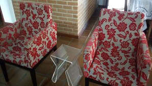 Two armchairs with floral upholstery, a small glass table, and a brick wall in the background. - Ótima casa com Wi-Fi a 350m da Praia de Peruíbe/SP (Peruíbe)