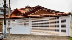 A house with a tiled roof, a white garage door, and a paved driveway. - Ótima casa com Wi-Fi a 350m da Praia de Peruíbe/SP (Peruíbe)