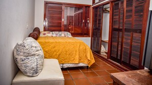 A bedroom with a bed, a nightstand, a wooden wardrobe, and a window with shutters. - Ótima casa com Wi-Fi a 350m da Praia de Peruíbe/SP (Peruíbe)