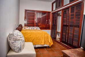 Ein Schlafzimmer mit einem Bett, einem Nachttisch, einem Holzschrank und einem Fenster mit Rollläden.