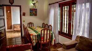 A dining area with a table set for four, surrounded by wooden chairs. A fan is mounted on the wall above the table. - Ótima casa com Wi-Fi a 350m da Praia de Peruíbe/SP (Peruíbe)