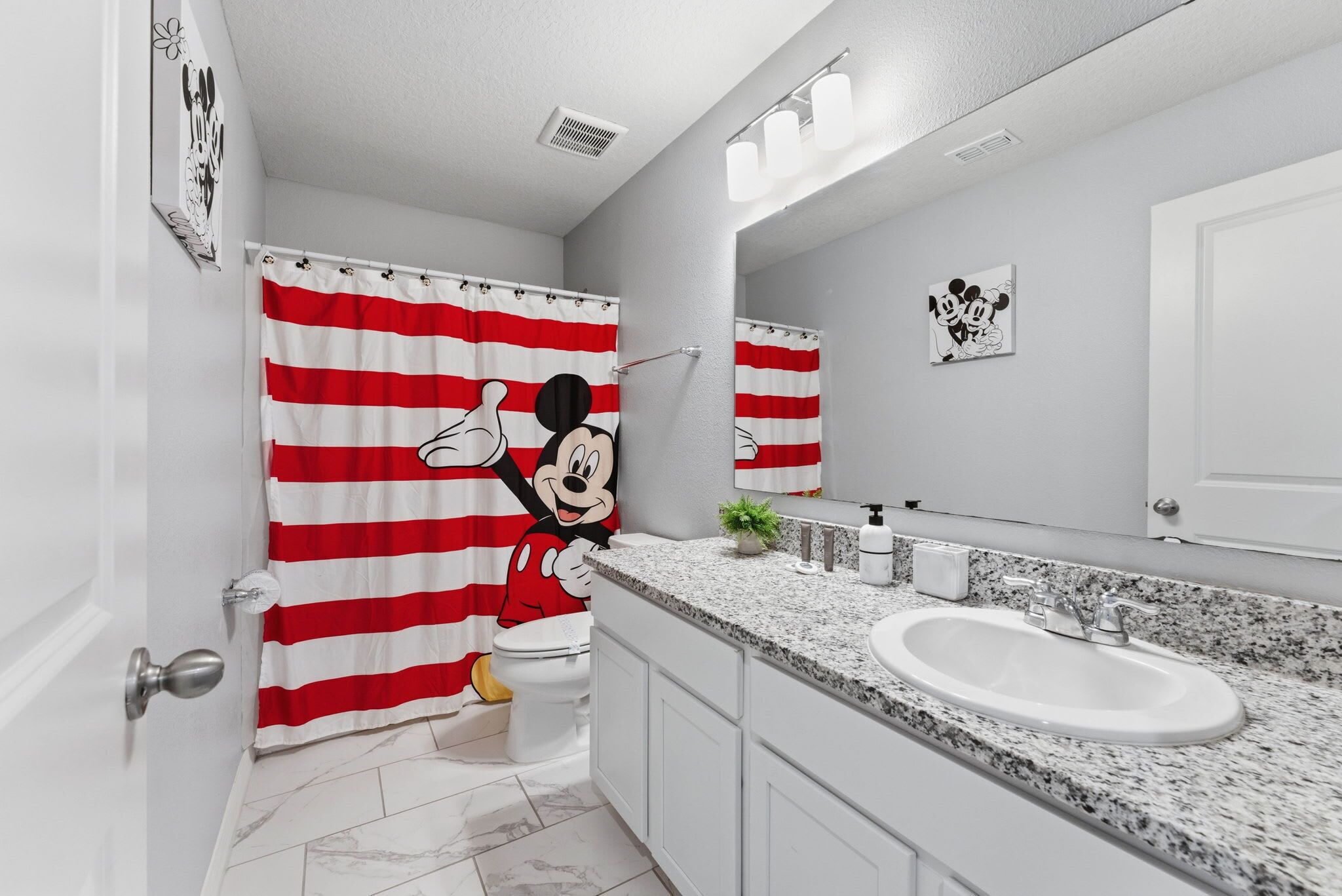 A bathroom with a Mickey Mouse shower curtain, a white sink, and a mirror.