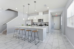 A modern kitchen with a central island, bar stools, white cabinets, and a microwave. - Savvy 4bed Stay Near Orlando Attractions (Kissimmee)