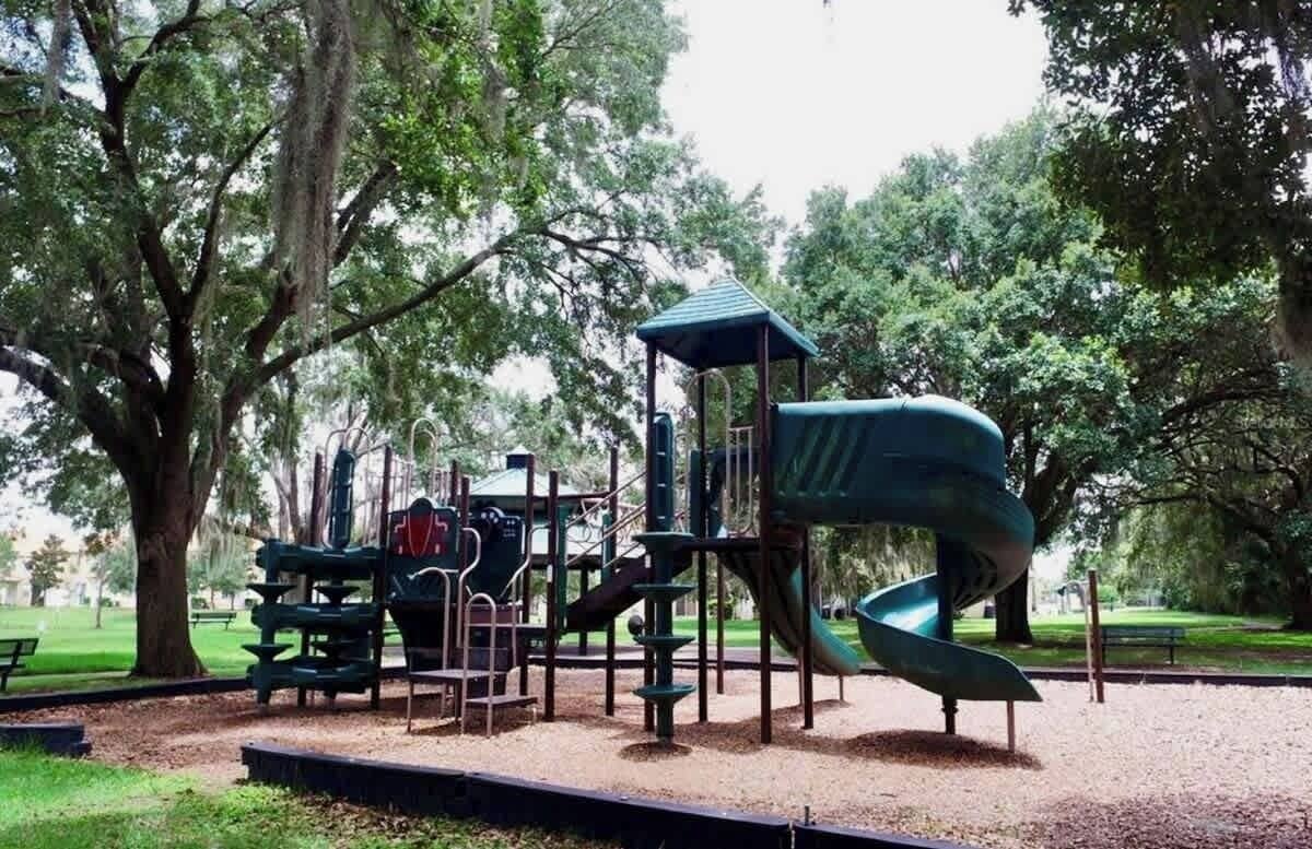 A playground with a spiral slide and climbing structures, surrounded by trees and a picnic area.