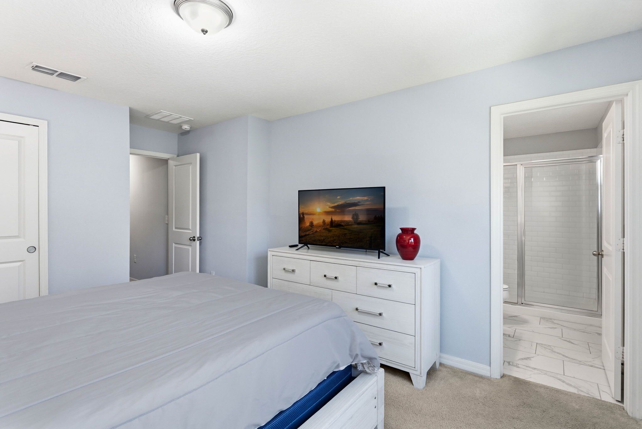 Ein Schlafzimmer mit Bett, Kommode, Fernseher und roter Vase.
