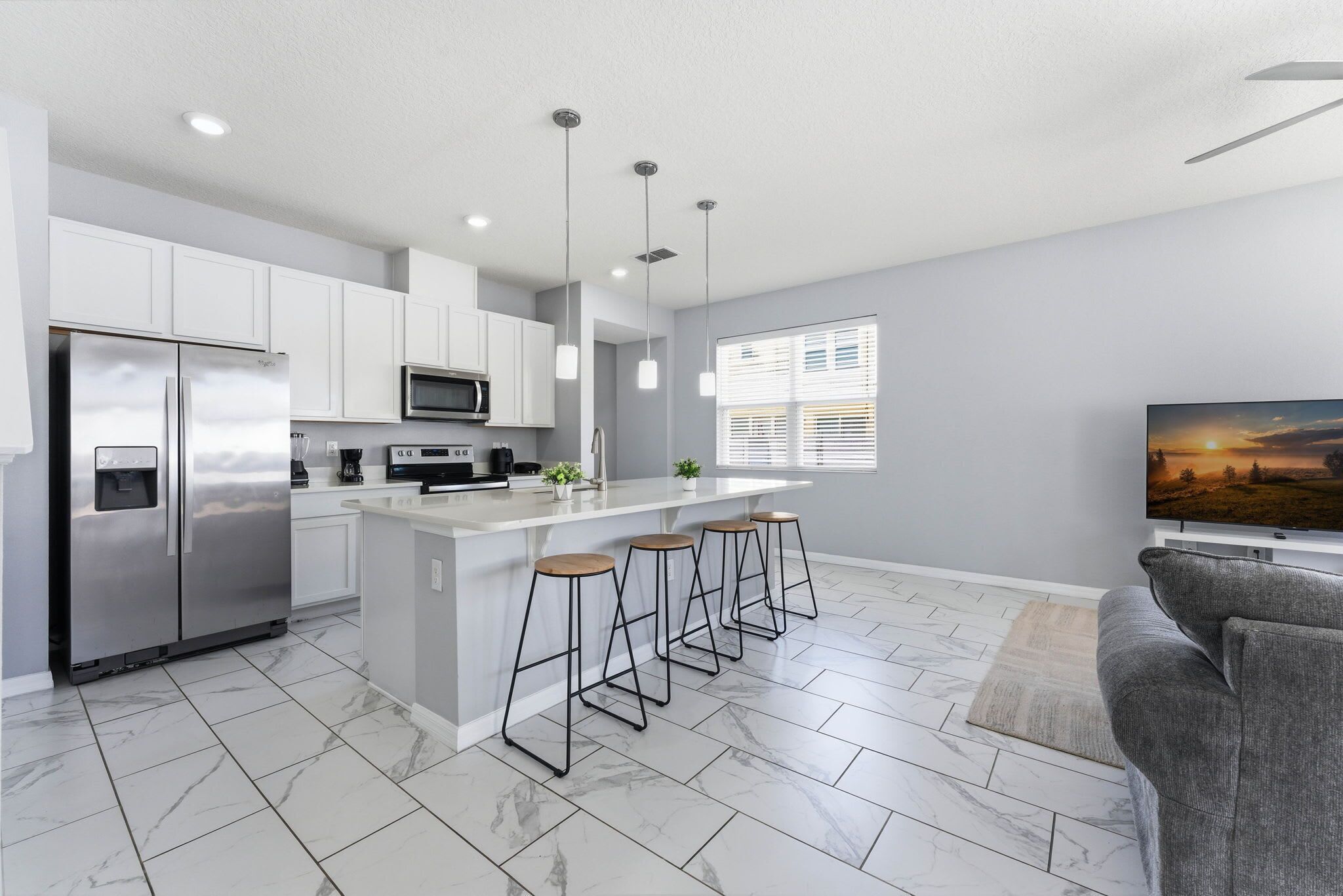 A modern kitchen with white cabinets, a stainless steel refrigerator, a microwave, and a bar area with stools.