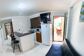 Uma cozinha compacta com geladeira, micro-ondas e um pequeno espaço de refeições com um banco.