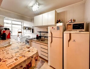 Eine Küche mit weißen Schränken, einem Kühlschrank, einer Mikrowelle und einer Kaffeemaschine.