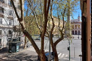 Straßenansicht mit Baumallee, einem historischen Gebäude und einer Kirche im Hintergrund.