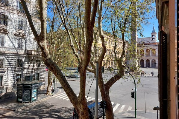 Vista de la calle con aceras arboladas, un edificio histórico y una iglesia al fondo.