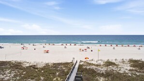 A beach with a wooden boardwalk leading to the shore, umbrellas, and beach chairs. - Shoalwater 405 (Orange Beach)