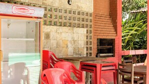 Un área de estar al aire libre con sillas y mesas de plástico rojo, un horno de ladrillo y un recinto de cristal con un cartel que dice 
