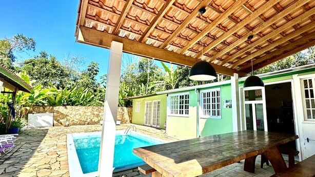 Un espacio exterior techado con piscina, una mesa de madera y un muro de piedra.