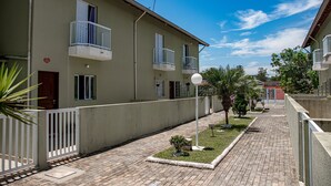 A residential building with a paved courtyard, a small garden, and a clear blue sky. - Casa c ótima localização e churrasq em Mongaguá/SP (Mongaguá)