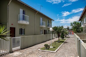 A residential building with a paved courtyard, a small garden, and a clear blue sky. - Casa c ótima localização e churrasq em Mongaguá/SP (Mongaguá)