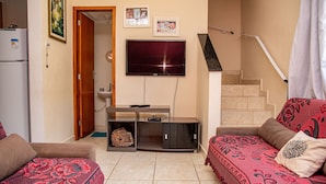 A living room with a TV, sofa, and a staircase. - Casa c ótima localização e churrasq em Mongaguá/SP (Mongaguá)