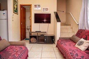 A living room with a TV, sofa, and a staircase. - Casa c ótima localização e churrasq em Mongaguá/SP (Mongaguá)