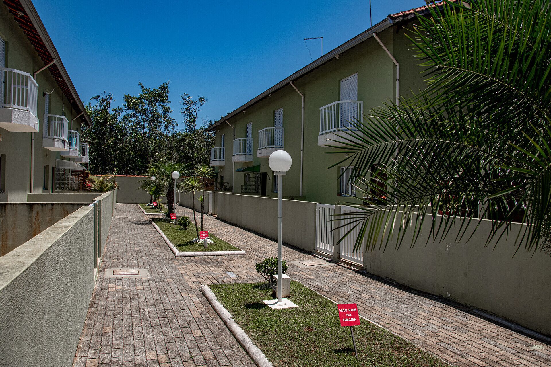 A residential area with paved walkways, a row of houses with balconies, and a clear blue sky.