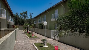 A residential area with a paved walkway, green lawns, and buildings with balconies. - Casa c ótima localização e churrasq em Mongaguá/SP (Mongaguá)