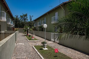 A residential area with a paved walkway, green lawns, and buildings with balconies. - Casa c ótima localização e churrasq em Mongaguá/SP (Mongaguá)
