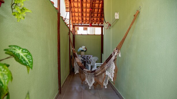 A narrow hallway with a hammock chair, a table with chairs, and a potted plant. - Casa c ótima localização e churrasq em Mongaguá/SP (Mongaguá)