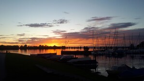 Satamassa on laivoja, etualalla on nurmialue ja taustalla auringonlasku.