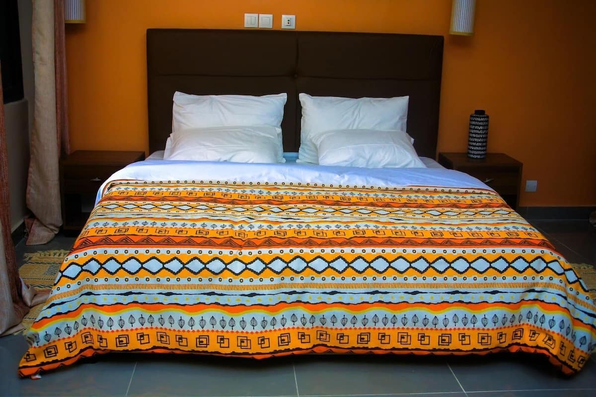 A bed with a patterned bedspread, two white pillows, and a nightstand with a lamp.
