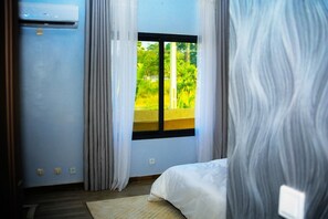 A bedroom with a bed, a window with a view of greenery, and an air conditioning unit on the wall. - Les Résidences Wilhelm (Yamoussoukro)