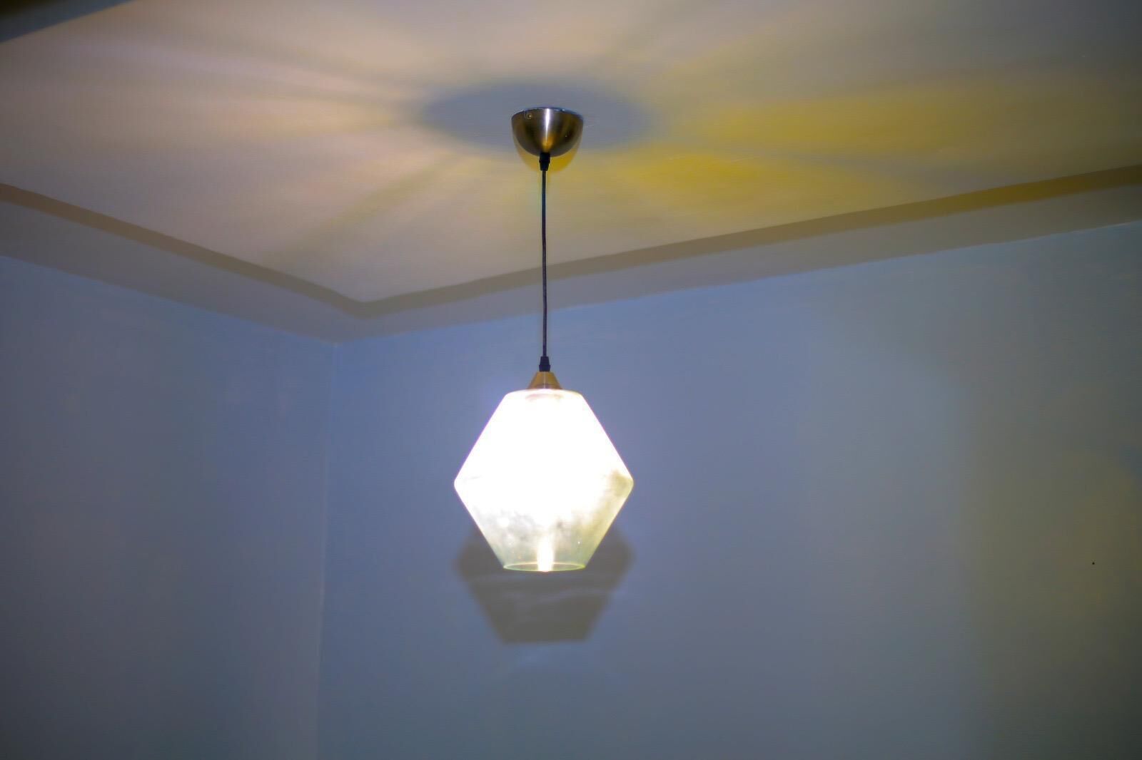 Eine sechseckige Pendelleuchte mit Metallfuß und Glaseinsatz, die an einer Decke hängt, von der ein weiterer Leuchten herabhängt.