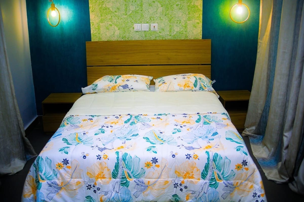 A bed with floral bedding, wooden headboard, and two wall-mounted lights.