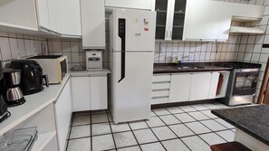 Una cocina con armarios blancos, refrigerador, cafetera, microondas y estufa.