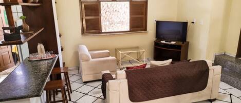 Una sala de estar con un sofá, televisor, una mesita y una ventana con contraventanas.