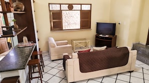 Una sala de estar con un sofá, televisor, una mesita y una ventana con contraventanas.