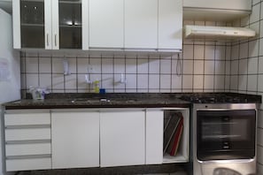 Una cocina con armarios blancos, encimera de granito, horno empotrado y un pequeño ventanal sobre el fregadero.