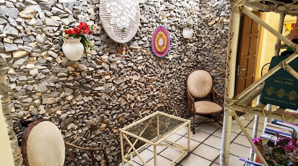 Una habitación con pared de piedra, una silla de mimbre, una mesita y una puerta con un letrero.