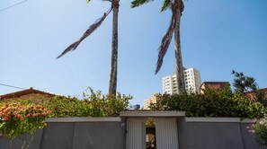A residential area with tall palm trees, a gated entrance, and a building in the background.