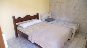 Una cama individual con cabecera de madera, una mesita de noche con lámpara blanca y una colcha estampada.