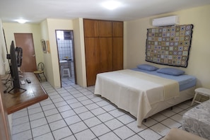 Una habitación con cama, escritorio, silla, armario y aire acondicionado.