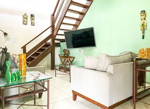 Ein Wohnzimmer mit einer Couch, einem Glastisch, einem an der Wand befestigten Fernseher, einer Treppe und Dekorationselementen.