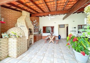 Eine Terrasse mit einem Backofen aus Ziegeln, einem Esstisch und Topfpflanzen.