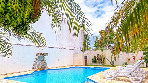 Una piscina amb una estructura de pedra, paviment de rajoles i seients de relax.