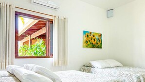 Habitació amb dos llits, una finestra amb cortines, un quadre de girassols i un aparell d'aire condicionat.