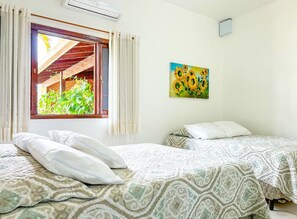 Ein Zimmer mit zwei Betten, einem Vorhangfenster, einem Sonnenblumenbild und einer Klimaanlage.